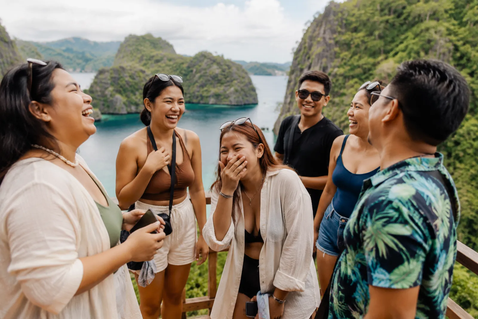 A group of Filipino travelers laughing together on a scenic tropical viewpoint overlooking limestone islands